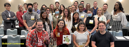 Group photo of attendees of the DiverseScholar Postdoctoral Conference. Roughly 3 rows of a diverse group of people are facing camera. First row of 4 people are sitting with one holding placard of DiverseScholar turtle logo. Around 25 people in second and third rows are standing with some wearing face masks. In lower left corner is the label in yellow text "DivSch24 Conference".